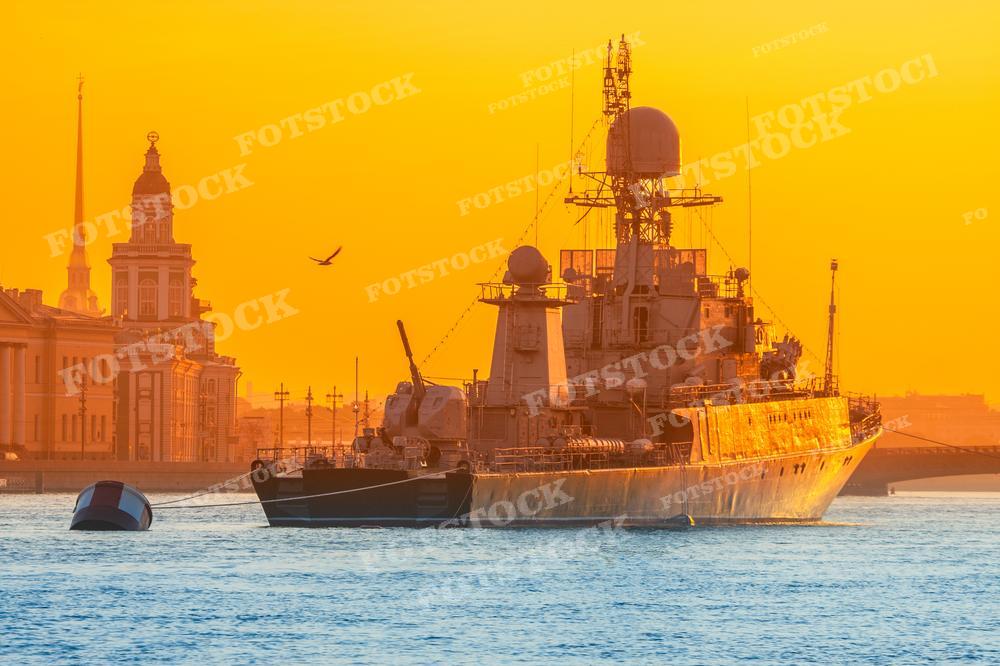На фотографии изображен военный корабль, пришвартованный на реке Неве в Санкт-Петербурге. Это часть военного парада кораблей в России. Утренняя атмосфера Петербурга придает особый шарм этому событию. Изображение может быть использовано для иллюстрации военных парадов, городских праздников и красивых пейзажей у реки. Оно также подходит для использования в тематических публикациях о военном флоте, городе Санкт-Петербурге и исторических моментах.